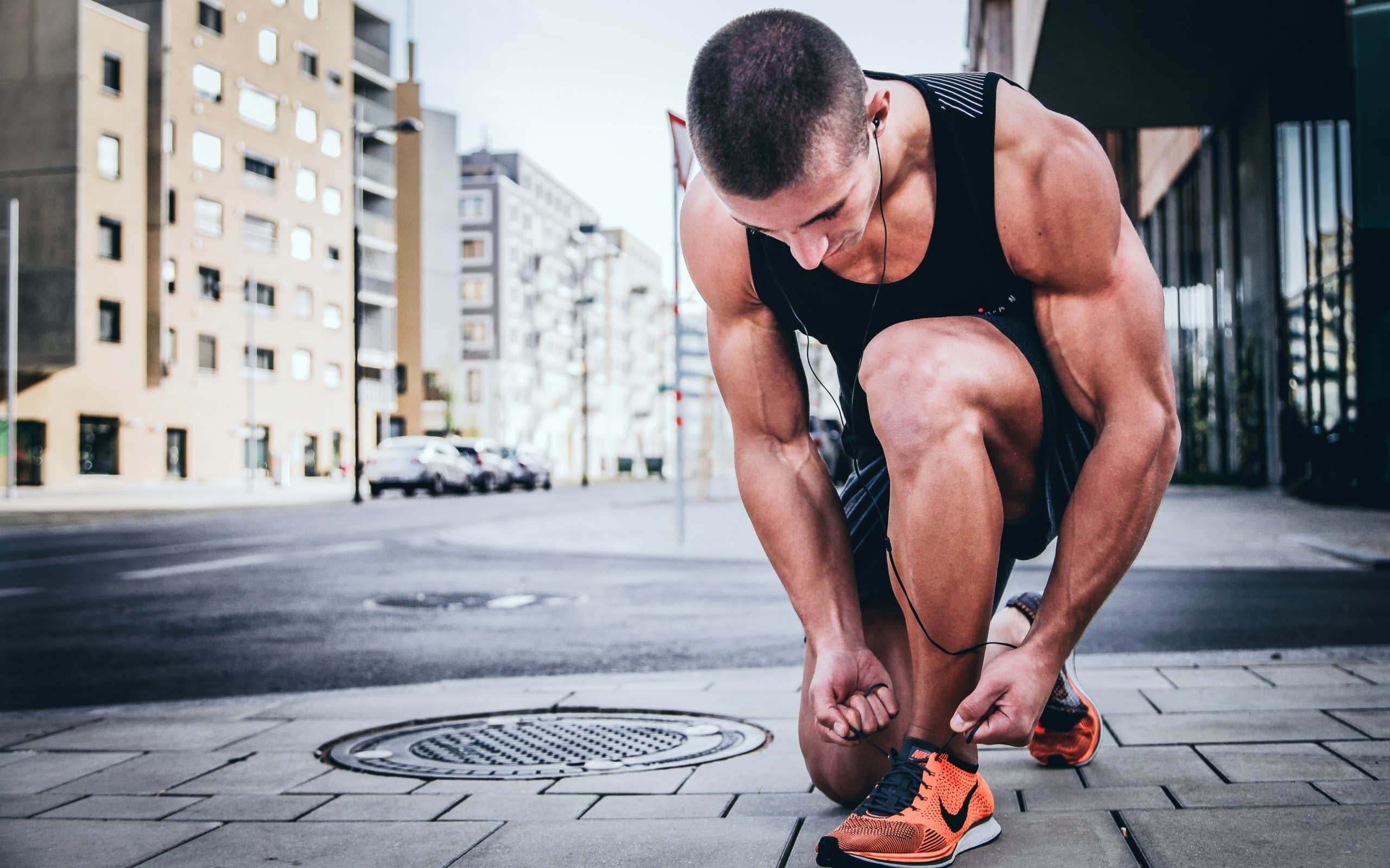 Homme en train de faire du sport dans la rue agenouillé pour refaire son lacet