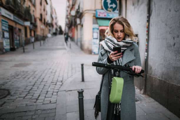 Jeune femme qui démarre une trottinette électrique grâce à son smartphone en plein centre ville